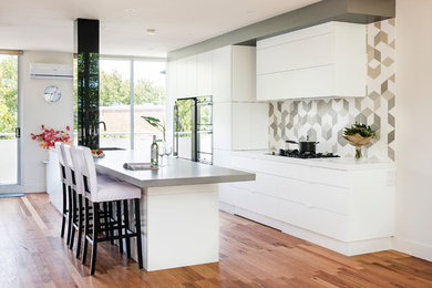 Inspiration for a contemporary galley eat-in kitchen in Melbourne with an integrated sink, white cabinets, quartz benchtops, grey splashback, mosaic tile splashback, black appliances, medium hardwood floors and with island.