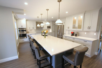 Eat-in kitchen - large contemporary l-shaped vinyl floor and brown floor eat-in kitchen idea in Toronto with an undermount sink, recessed-panel cabinets, white cabinets, quartz countertops, gray backsplash, subway tile backsplash, stainless steel appliances, an island and white countertops