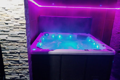 This is an example of a contemporary back custom shaped hot tub in Other with tiled flooring.