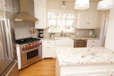 Example of a mid-sized transitional l-shaped light wood floor and brown floor enclosed kitchen design in San Diego with a farmhouse sink, raised-panel cabinets, white cabinets, granite countertops, gray backsplash, subway tile backsplash, stainless steel appliances and a peninsula