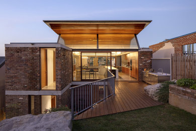 This is an example of a large contemporary backyard deck in Sydney with an outdoor kitchen and a roof extension.