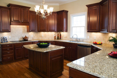 Example of a mid-sized classic u-shaped medium tone wood floor and brown floor enclosed kitchen design in Philadelphia with an undermount sink, dark wood cabinets, granite countertops, beige backsplash, ceramic backsplash, stainless steel appliances and an island