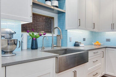 Large transitional l-shaped medium tone wood floor and brown floor kitchen photo in Chicago with a farmhouse sink, shaker cabinets, white cabinets, quartzite countertops, blue backsplash, glass tile backsplash, stainless steel appliances and an island