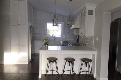 Small transitional u-shaped medium tone wood floor and brown floor kitchen photo in Toronto with flat-panel cabinets, white cabinets, quartz countertops, white backsplash, ceramic backsplash, stainless steel appliances and a peninsula