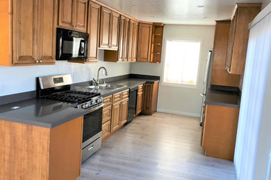 Inspiration for a mid-sized timeless galley laminate floor and beige floor enclosed kitchen remodel in San Francisco with a drop-in sink, raised-panel cabinets, medium tone wood cabinets, quartz countertops, stainless steel appliances, no island and black countertops