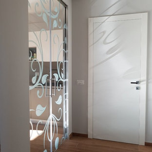 Immagine di un piccolo ingresso contemporaneo con pareti grigie, pavimento in gres porcellanato, una porta singola, una porta bianca e pavimento marrone