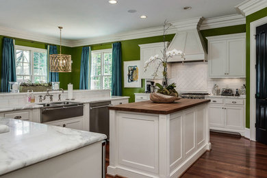 Elegant u-shaped dark wood floor kitchen photo in Charlotte with a farmhouse sink, recessed-panel cabinets, white cabinets, white backsplash, subway tile backsplash, stainless steel appliances and an island