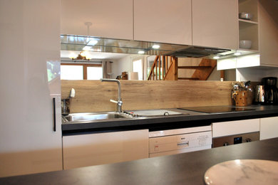 Cette image montre une cuisine ouverte chalet en L de taille moyenne avec des portes de placard blanches, une crédence miroir, îlot et plan de travail noir.