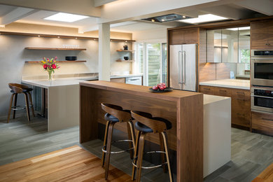 This is an example of a midcentury u-shaped eat-in kitchen in San Francisco with an undermount sink, flat-panel cabinets, dark wood cabinets, solid surface benchtops, grey splashback, mirror splashback, stainless steel appliances, porcelain floors, with island, grey floor and beige benchtop.