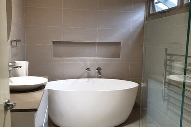 This is an example of a large contemporary master bathroom in Sydney with furniture-like cabinets, white cabinets, a freestanding tub, an open shower, beige tile, porcelain tile, beige walls, porcelain floors, a vessel sink, engineered quartz benchtops, beige floor, a hinged shower door and beige benchtops.