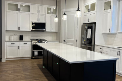 Example of a mid-sized trendy l-shaped medium tone wood floor, brown floor and vaulted ceiling eat-in kitchen design in Portland with an undermount sink, shaker cabinets, white cabinets, quartz countertops, white backsplash, subway tile backsplash, stainless steel appliances, an island and white countertops