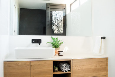 Small modern master bathroom in Canberra - Queanbeyan with furniture-like cabinets, medium wood cabinets, a drop-in tub, a shower/bathtub combo, a wall-mount toilet, white tile, white walls, ceramic floors, engineered quartz benchtops, black floor, an open shower and white benchtops.