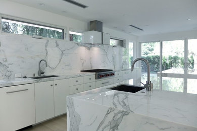 Large minimalist single-wall light wood floor eat-in kitchen photo in Other with an undermount sink, flat-panel cabinets, white cabinets, marble countertops, white backsplash, stone slab backsplash, stainless steel appliances and two islands