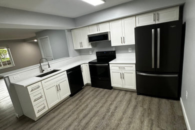 Minimalist vinyl floor and gray floor kitchen photo in Baltimore with a drop-in sink, shaker cabinets, white cabinets, quartz countertops, white backsplash, quartz backsplash, black appliances and white countertops