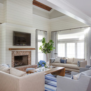 Beach style medium tone wood floor and brown floor family room photo in Jacksonville with white walls, a standard fireplace, a brick fireplace and a wall-mounted tv
