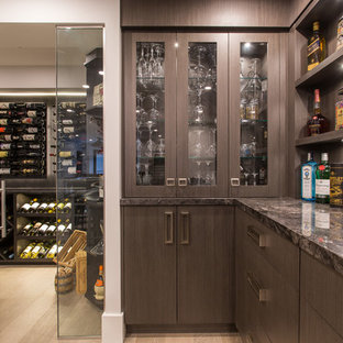 バンクーバーの大きいトランジショナルスタイルのおしゃれな着席型バー (アンダーカウンターシンク、家具調キャビネット、茶色いキャビネット、大理石カウンター、グレーのキッチンパネル、石タイルのキッチンパネル、無垢フローリング、ベージュの床、黒いキッチンカウンター) の写真