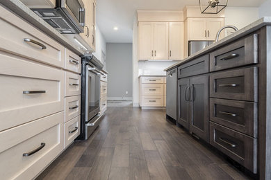 Mid-sized l-shaped medium tone wood floor and multicolored floor open concept kitchen photo in Edmonton with a double-bowl sink, recessed-panel cabinets, beige cabinets, quartz countertops, white backsplash, ceramic backsplash, stainless steel appliances and an island
