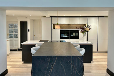 Photo of a large modern grey and white kitchen/diner in Other with white cabinets, quartz worktops, integrated appliances, multiple islands, grey floors, grey worktops and feature lighting.