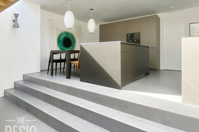 Inredning av ett modernt mellanstort vit vitt kök med öppen planlösning, med släta luckor, bruna skåp, marmorbänkskiva, betonggolv, en köksö och grått golv