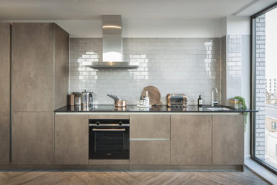 Design ideas for a small contemporary grey and white galley open plan kitchen in Manchester with a submerged sink, flat-panel cabinets, distressed cabinets, composite countertops, white splashback, cement tile splashback, black appliances, laminate floors, a breakfast bar and white worktops.