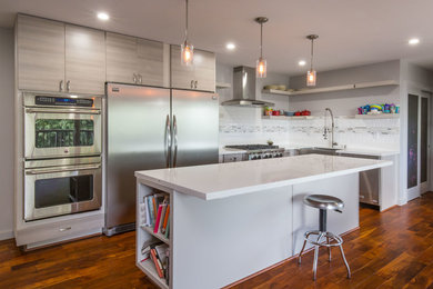 Large trendy l-shaped medium tone wood floor open concept kitchen photo in Orange County with a farmhouse sink, flat-panel cabinets, gray cabinets, quartzite countertops, white backsplash, subway tile backsplash, stainless steel appliances and an island