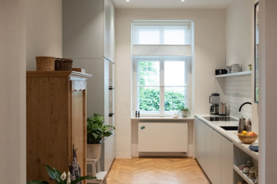 ミュンヘンにある小さな北欧スタイルのおしゃれなI型キッチン (一体型シンク、フラットパネル扉のキャビネット、青いキャビネット、大理石カウンター、白いキッチンパネル、サブウェイタイルのキッチンパネル、黒い調理設備、無垢フローリング、ベージュのキッチンカウンター) の写真