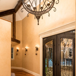 Cette photo montre un grand hall d'entrée éclectique avec un mur beige, un sol en brique, une porte double et une porte noire.