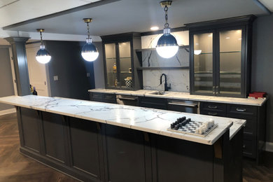 Minimalist light wood floor and brown floor wet bar photo in New York with a drop-in sink, glass-front cabinets, blue cabinets, marble countertops, white backsplash, marble backsplash and white countertops