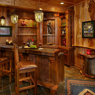 他の地域の大きいラスティックスタイルのおしゃれな着席型バー (スレートの床、落し込みパネル扉のキャビネット、濃色木目調キャビネット) の写真