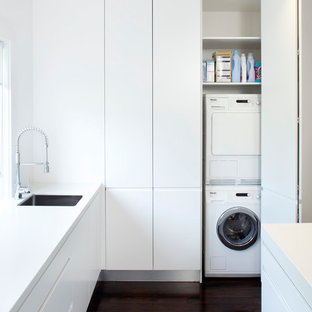 Photo of a modern utility room in Sydney with white cabinets and a concealed washer and dryer.