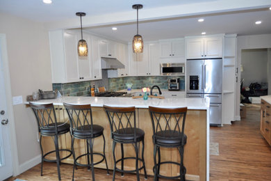 Example of a mid-sized transitional bamboo floor eat-in kitchen design in New York with an undermount sink, recessed-panel cabinets, white cabinets, quartz countertops, green backsplash, porcelain backsplash, stainless steel appliances, a peninsula and white countertops