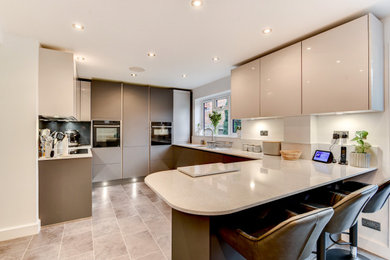 Design ideas for a large modern u-shaped open plan kitchen in Sussex with an undermount sink, flat-panel cabinets, grey cabinets, quartzite benchtops, grey splashback, glass sheet splashback, panelled appliances, vinyl floors, a peninsula, grey floor and white benchtop.