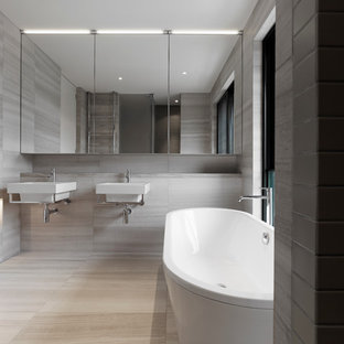 Immagine di una stanza da bagno moderna con lavabo sospeso, ante lisce, top in travertino, vasca freestanding, lastra di pietra, pareti grigie e pavimento in travertino