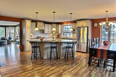 Example of a large farmhouse u-shaped travertine floor open concept kitchen design in Toronto with a double-bowl sink, raised-panel cabinets, distressed cabinets, granite countertops, beige backsplash, stone tile backsplash, stainless steel appliances and an island