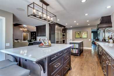 Example of a large classic medium tone wood floor and brown floor eat-in kitchen design in St Louis with an undermount sink, recessed-panel cabinets, dark wood cabinets, quartz countertops, white backsplash, subway tile backsplash, stainless steel appliances, two islands and white countertops