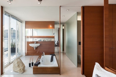 Photo of a mid-sized contemporary master bathroom in Munich with a wall-mount sink, a drop-in tub, a wall-mount toilet, beige tile, stone slab and grey walls.
