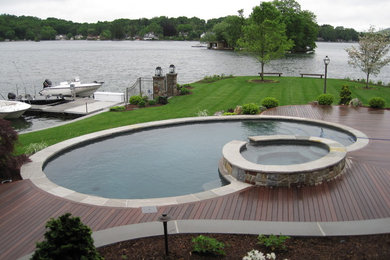 This is an example of a large arts and crafts backyard round natural pool in New York with a hot tub and decking.