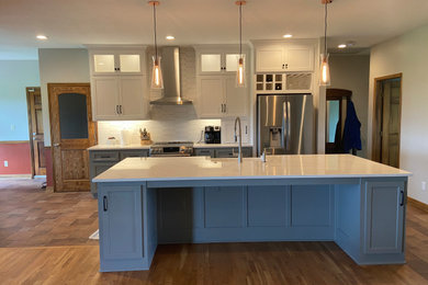 Inspiration for a transitional porcelain tile kitchen remodel in Kansas City with a farmhouse sink, recessed-panel cabinets, white cabinets, quartz countertops, white backsplash, ceramic backsplash, stainless steel appliances and an island