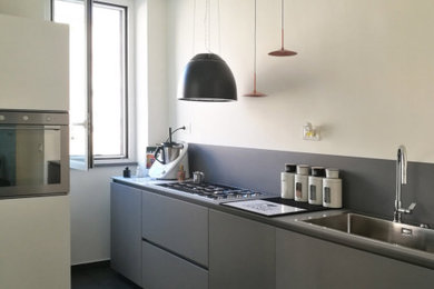 Ispirazione per una cucina contemporanea con lavello a vasca singola, ante lisce, ante grigie, paraspruzzi grigio, elettrodomestici neri, pavimento in gres porcellanato, pavimento grigio, top grigio e travi a vista