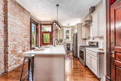 Eat-in kitchen - mid-sized traditional single-wall medium tone wood floor and brown floor eat-in kitchen idea in St Louis with a farmhouse sink, shaker cabinets, beige cabinets, glass countertops, beige backsplash, ceramic backsplash, stainless steel appliances, an island and white countertops