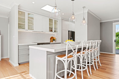 Photo of a large galley kitchen pantry in Sydney with a double-bowl sink, shaker cabinets, grey cabinets, white splashback, ceramic splashback, stainless steel appliances, light hardwood floors, with island, multi-coloured floor and white benchtop.