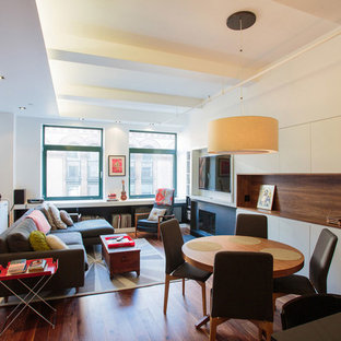 Idéer för små funkis allrum med öppen planlösning, med en standard öppen spis, en väggmonterad TV, mellanmörkt trägolv, en spiselkrans i metall, vita väggar och brunt golv