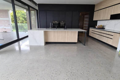 Inspiration for a mid-sized contemporary l-shaped open plan kitchen in Melbourne with an undermount sink, flat-panel cabinets, light wood cabinets, marble benchtops, white splashback, marble splashback, black appliances, concrete floors, with island, grey floor and white benchtop.