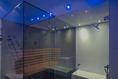 Mittelgroße Moderne Sauna mit flächenbündigen Schrankfronten, weißen Schränken, Einbaubadewanne, bodengleicher Dusche, Wandtoilette, weißer Wandfarbe, Mineralwerkstoff-Waschtisch, schwarzem Boden, Falttür-Duschabtrennung und weißer Waschtischplatte in Düsseldorf