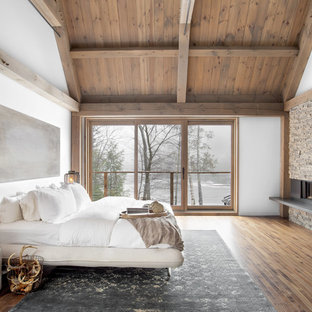 Exemple d'une chambre montagne avec un mur blanc, un sol en bois brun, une cheminée ribbon et un sol marron.