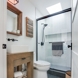Cette photo montre une salle d'eau bord de mer avec un placard à porte plane, des portes de placard en bois clair, une baignoire d'angle, un carrelage blanc, des plaques de verre, un mur bleu, un lavabo posé, un WC à poser et une cabine de douche à porte coulissante.
