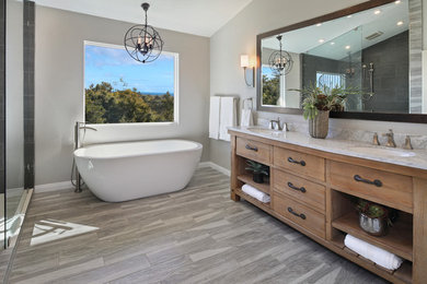 This is an example of a mid-sized contemporary master bathroom in Orange County with flat-panel cabinets, medium wood cabinets, a freestanding tub, an open shower, a one-piece toilet, porcelain tile, grey walls, medium hardwood floors, an undermount sink, marble benchtops, grey floor and an open shower.