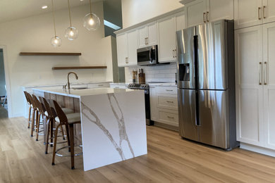 Large trendy l-shaped eat-in kitchen photo in Other with shaker cabinets, white cabinets, quartz countertops, white backsplash, subway tile backsplash and an island