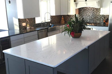 Example of a mid-sized transitional l-shaped dark wood floor and black floor kitchen design in Minneapolis with a farmhouse sink, shaker cabinets, white cabinets, quartzite countertops, multicolored backsplash, mosaic tile backsplash, stainless steel appliances and an island