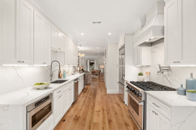 Cette photo montre une cuisine moderne avec un évier posé, des portes de placard blanches, une crédence blanche, un électroménager en acier inoxydable, un sol en bois brun, un sol beige et un plan de travail blanc.
